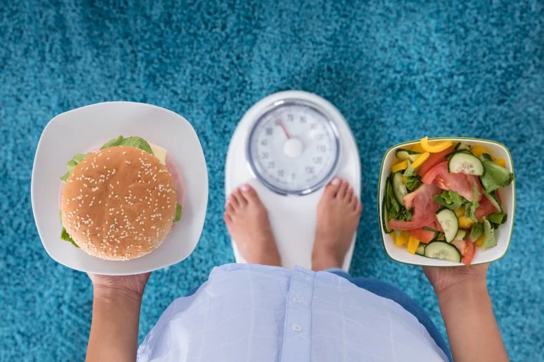 Person Holding Burger and Salad Standing On Scale