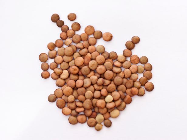 A pile of brown lentils on a white background.