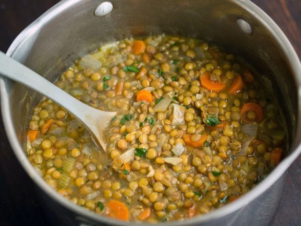 A pot of vegan lentil soup with onion, carrots, celery and garnished with parsley.
