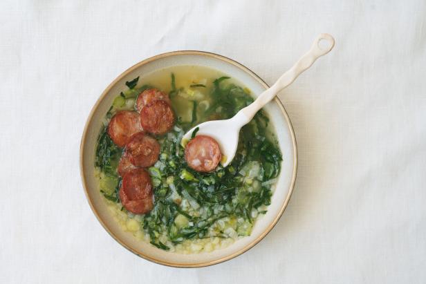 Caldo Verde Soup with greens and chopped chorizo on the top in ceramic bowl with ceramic spoon. Top View