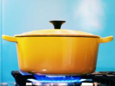 A yellow enamel casserole, with its lid on, sits on a lit gas burner creating steam as it heats.
