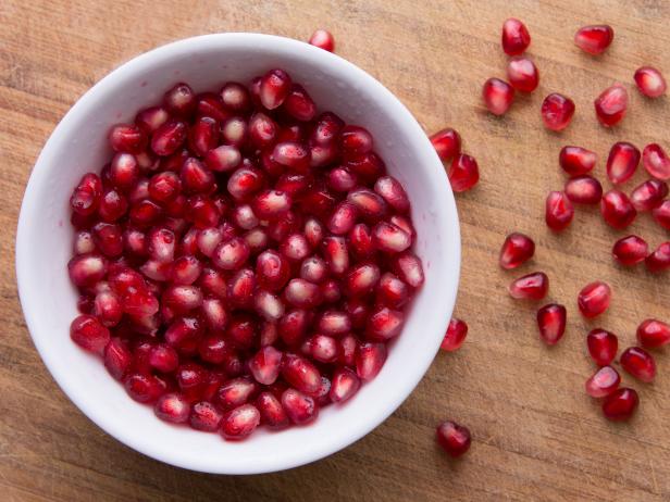 Pomegranate seeds are in a white bowl on the old cutting board