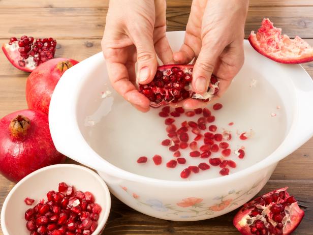 Hands seeding a pomegranate with the water method