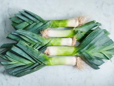Collection of leeks with roots and leaves attached, arranged on a white marble surface.
