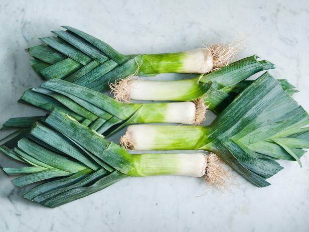 Collection of leeks with roots and leaves attached, arranged on a white marble surface.