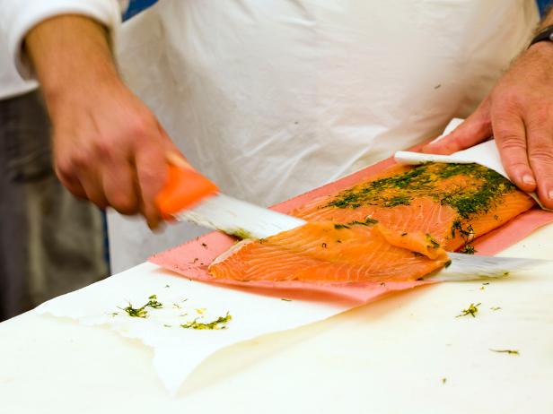 Fish monger cuts thin slices of smoked salmon (lox).