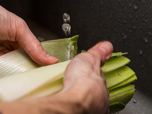 Close up of unrecognizable chef washing and rinsing the mud off an organic leek under cold running water.