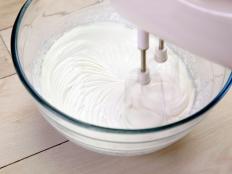 Whipping cream mixer in a glass bowl on wooden table
