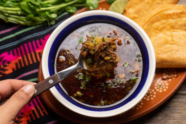 Traditional mexican birria consome soup and tacos on wooden background