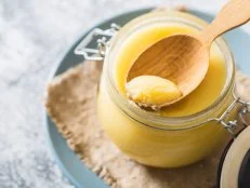 Ghee or clarified butter in jar and wooden spoon on gray table. Top view. Copyspace. Ghee butter have healthy fat and is a common cooking ingredient in many of the Indian food