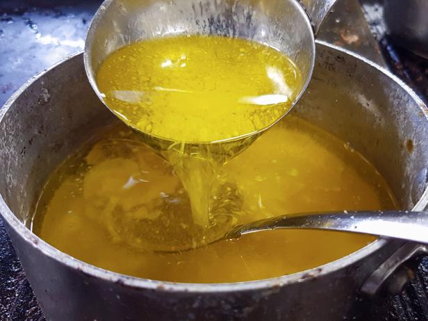 Pouring yellow, melted, clarified butter, back down to the casserol, at a restaurant kitchen