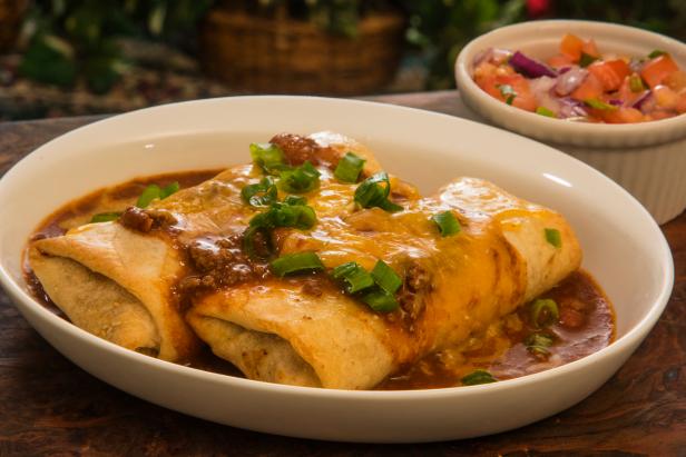 two beef chimichanga topped with chili gravy melted cheddar cheese and green onions with salsa on the side