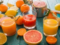 verschiedene Fruchtsäfte (Orange, Blutorange, Mehrfrucht) und Zitrusfrüchte (Grapefruits, Mandarinen, Zitronen), Saftpresse, blauer Holztisch, Studio