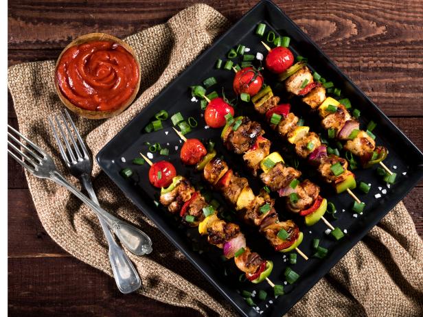 Grilled chicken skewers with spices and vegetables in a pan on a wooden background. Top view.