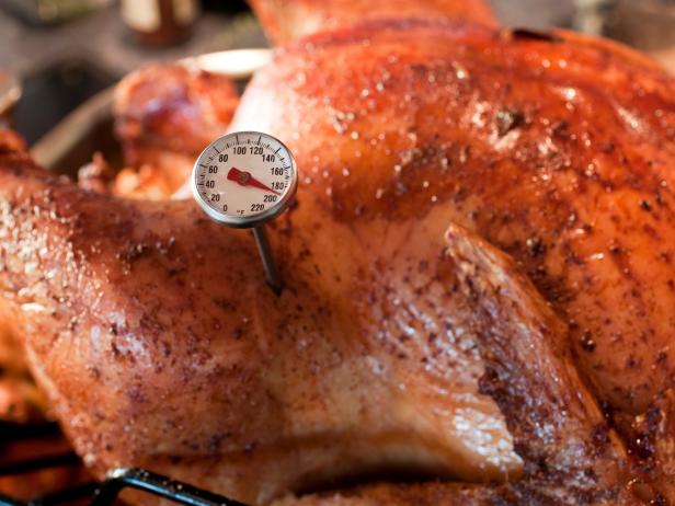 Roasted Turnkey fresh out of the oven. There is a little meat thermometer in the bird that reads 180 Roasted Turnkey fresh out of the oven. There is a little meat thermometer in the bird that reads 180?. The Fowl is Ready! This shot has a pretty narrow depth of field, focussing on the temperature gauge. The texture of the skin is fantastic and indicative of a perfectly cooked Thanksgiving turkey. The background has blurry kitchen elements in it.  - A great shot for preparation cookbooks, ingredient, catalogs, chef, diet and cooking websites or magazines  The bird is in a roasting Pan