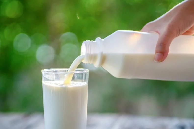 Pouring milk in the glass on the background of nature.