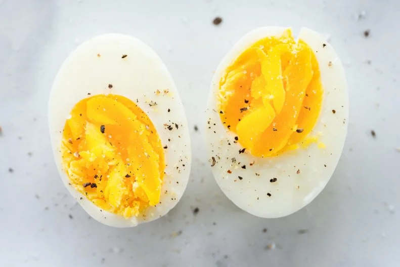 Hard boiled eggs cut in half and seasoned with salt and pepper on marble surface.