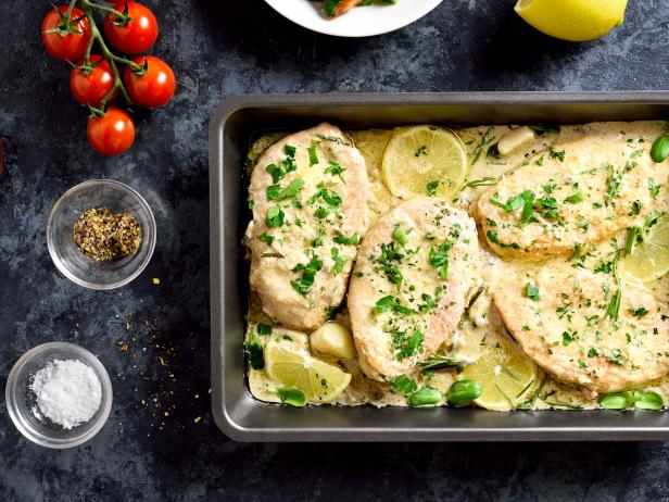 Chicken breast in creamy garlic sauce in baking dish over blue stone background. Healthy diet food. Top view, flat lay