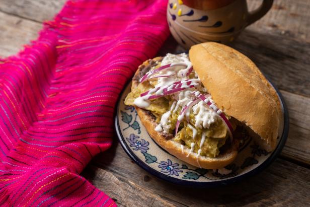 Traditional mexican green chilaquiles sandwich with cheese also called "guajolota" or "torta de chilaquiles" on wooden background