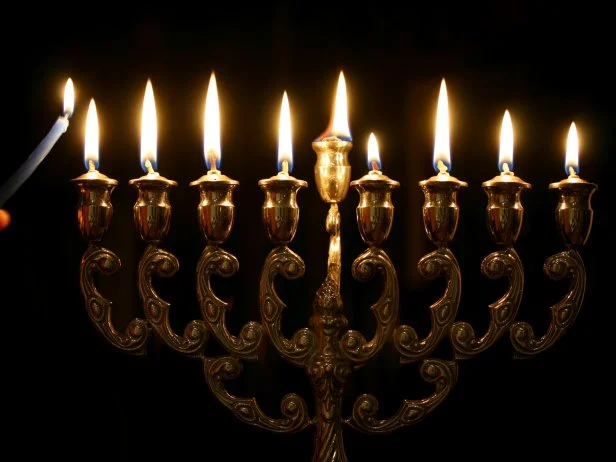 Lighting the menorah. Hand holding candle has motion blur.
