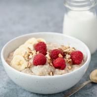 Bowl of oatmeal porridge with raspberries and banana slices. Milk oatmeal porridge in bowl