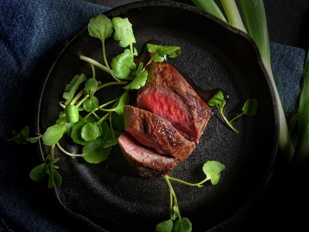 Pan-fried fillet of venison in wrought-iron black skillet with watercress salad garnish. Shot overhead. Generous accommodation for copy space.