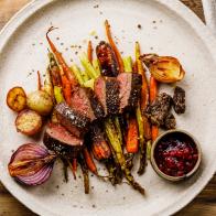 Grilled sliced Venison Steak with baked vegetables and berry sauce on wooden background