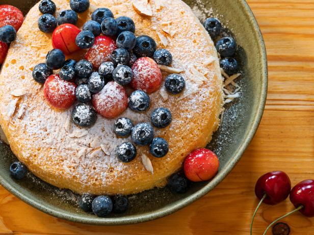 Summer sponge cake with fresh sweet cherries, blueberries, almonds and sugar powder  over wood rustic table, close up