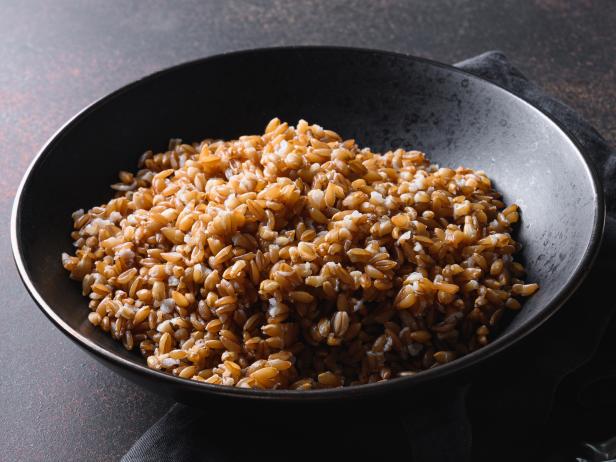 Cooked Whole Grain cereal spelt in black bowl on dark brown background. Close up. Space for text.