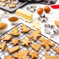Overhead view of a white background filled with ingredients for preparing Christmas cookies. A cooling rack and a baking sheet with fresh baked cookies complete the composition. High resolution 42Mp studio digital capture taken with SONY A7rII and Zeiss Batis 40mm F2.0 CF lens