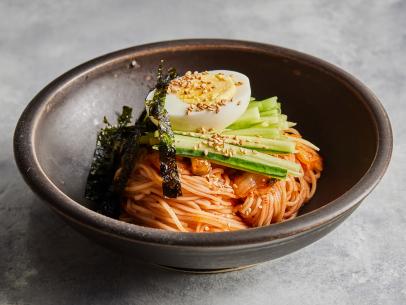 Description: Food Network Kitchen's Kimchi Bibim Guksu. Keywords: Kimchi, Sugar, Gochujang, Rice Vinegar, Soy Sauce, Minced Garlic, Gochugaru, Somyeon, English Cucumber, Roasted Seaweed, Egg, Toasted Sesame Seeds.
