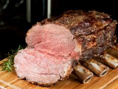 SEVERAL MORE IN THIS SERIES. Roasted prime rib cooked medium rare and juicy.  Also known as a standing rib roast; this is the cut from which ribeye steaks are made.  Wine glasses and bottle in background.  Shallow DOF.