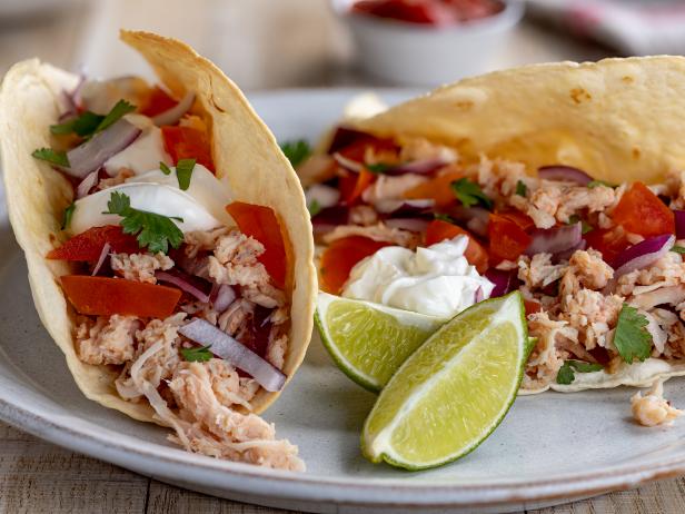 Tacos with pulled chicken, tomato, onion and sour cream and lime wedges on the side on a plate
