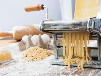 Side view of table full of pasta ingredients and pasta making tools on wooden background