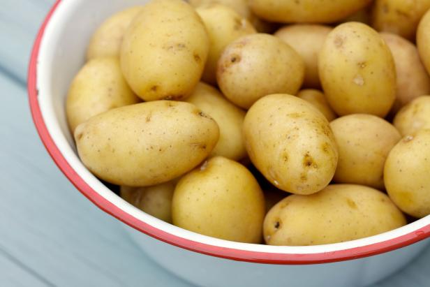 Natural light photo of raw small potatoes in metal bowl on wood table