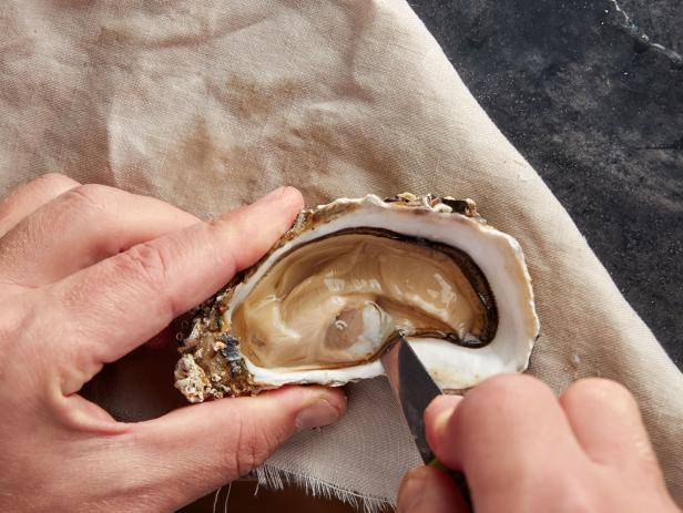 Man opening fresh oyster using knife and towel, top view