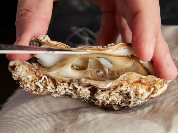 Man opening fresh oyster using knife and towel