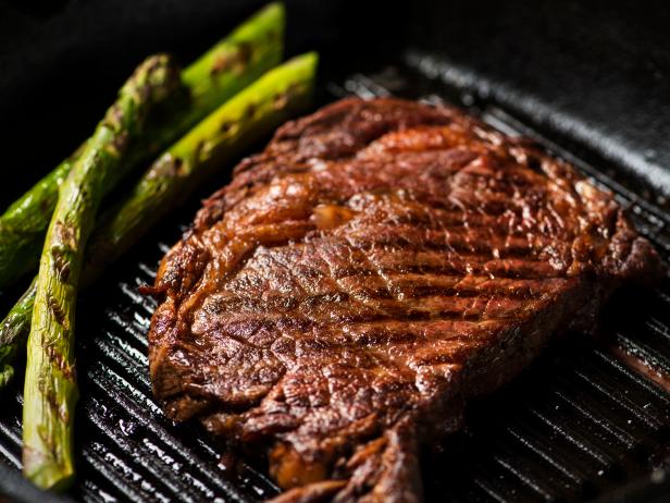 Ribeye steak with grill marks in a cast iron pan with asparagus.