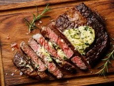 Sliced grilled Medium rare barbecue steak Ribeye with herb butter on cutting board close up
