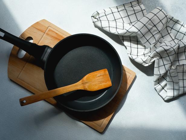 A New Clean Empty Cast-Iron Frying Pan And A Wooden spatula, on a cutting board. The concept of cooking in a restaurant and cafe, at home in the kitchen. Cook yourself, taking courses on the ability to cook delicious and beautiful food.