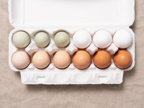Multi Colored Chicken Eggs in Carton on Beige Colored Linen Tablecloth.