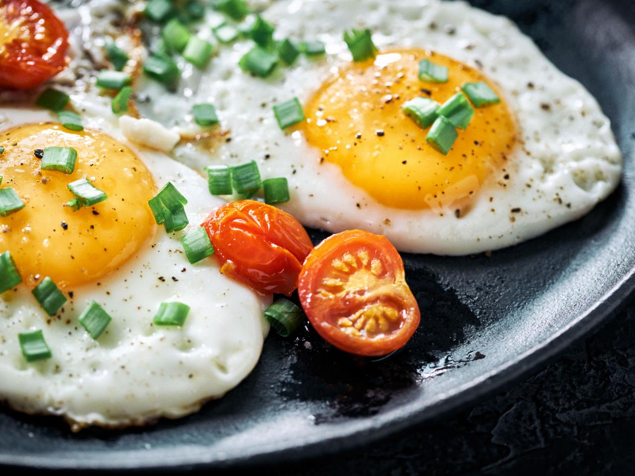 https://food.fnr.sndimg.com/content/dam/images/food/fullset/2022/01/03/sunny-side-up-egge-tomato-green-onion-black-plate.jpg.rend.hgtvcom.1280.960.suffix/1641186588350.jpeg