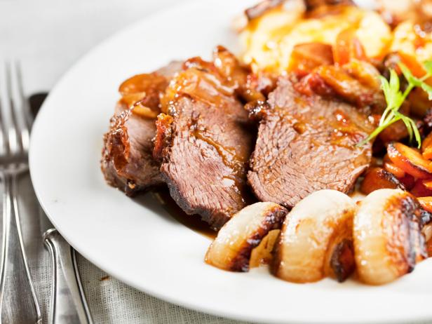 slices of roast beef on plate, surrounded by roast onoins and carrots