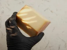 Gruyère au lait cru. Human hand in black disposable latex glove holding piece of gruyère. High point of view.