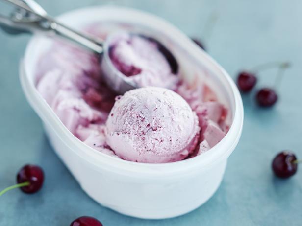 Tasty refreshing ice cream with cherry in plastic box on bright background. Closeup.