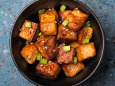 Top view of fried tofu with sesame seeds and green onion for healthy vegan and vegetarion nutrition on blue concrete background