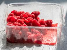 Raspberries in plastic supermarket tub packaging. Healthy ripe red organic fruit in shop bought recyclable container on kitchen worktop.