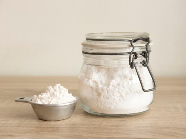 White flour in a measuring cup and transparent jar at the center on a wood table."n