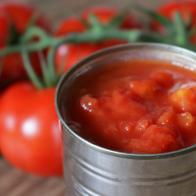 Stock Photo of unbranded generic tin of chopped tomatoes pieces / canned passata from supermarket with large vine tomato plant on wooden chopping board / bread board, diced and chopped Italian tinned tomatoes puree juice, peeled for ragu pasta sauce with garlic
