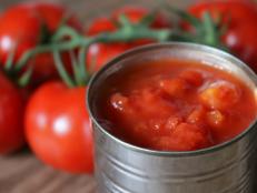 Stock Photo of unbranded generic tin of chopped tomatoes pieces / canned passata from supermarket with large vine tomato plant on wooden chopping board / bread board, diced and chopped Italian tinned tomatoes puree juice, peeled for ragu pasta sauce with garlic